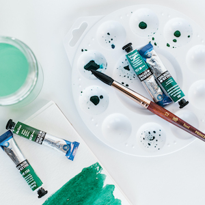 A paintbrush on a round palette with tubes of watercolor paint