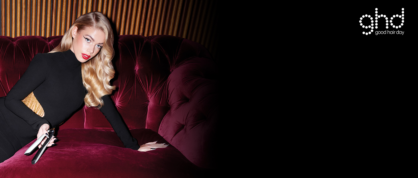 blonde model holding ghd platinum+ styler in white on a red velvet couch