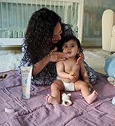 baby on a blanket next to a bottle of skin cream