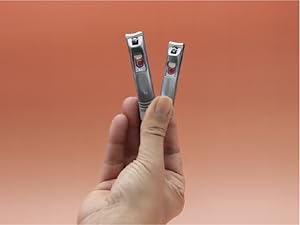 A person grips two Cuticor nail clippers in their fingers in front of an orange background.