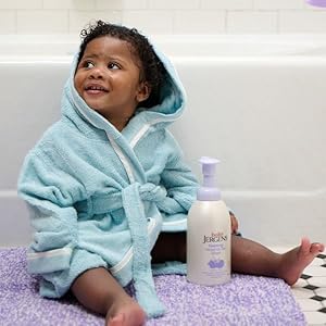 Baby sitting next to bath tub holding bottle of Baby Jergens foaming wash.