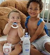 A baby sitting next to a toddler and a bottle of lotion