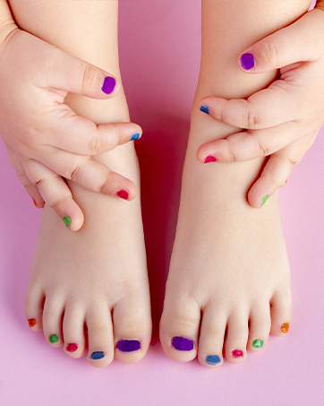 Hands and feet displayed on pink background showcasing multicolored nail polish in various bright shades including purple, blue, red, and green.