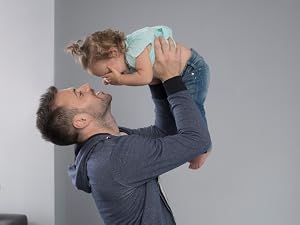 Man in navy sweatshirt lifting toddler in light blue tee-shirt and jeans into the air 