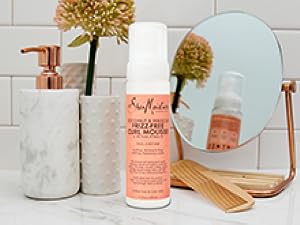 SheaMoisture Curl Mousse bottle on white marble bathroom counter with white tiles and accessories.