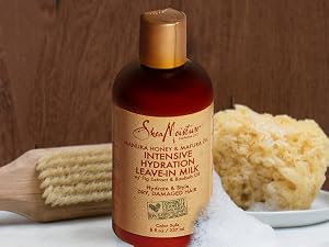 SheaMoisture leave-in milk bottle with shower accessories and soap on a wooden background.