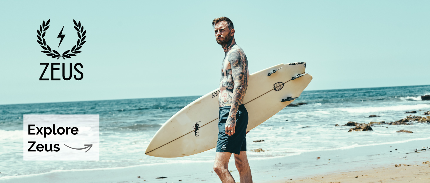bearded man standing on beach with surfboard